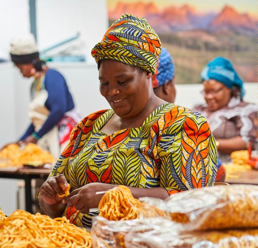 Woman in colorful traditional attire working with food at a market stall.
