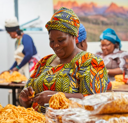 Woman in colorful traditional attire working with food at a market stall.