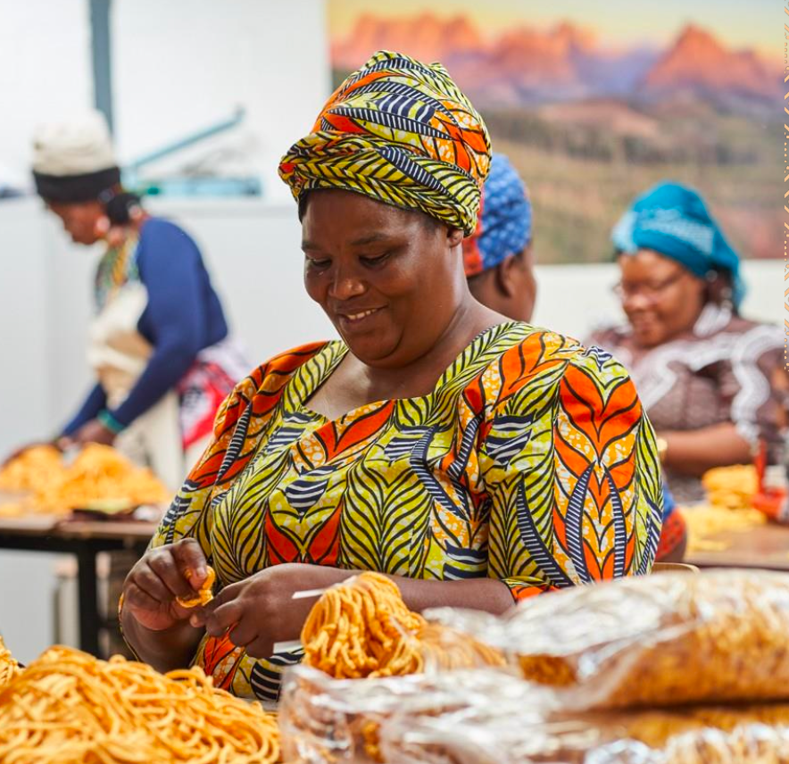 Woman in colorful traditional attire working with food at a market stall.