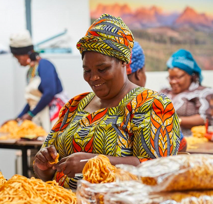 Woman in colorful traditional attire working at a market stall with food.