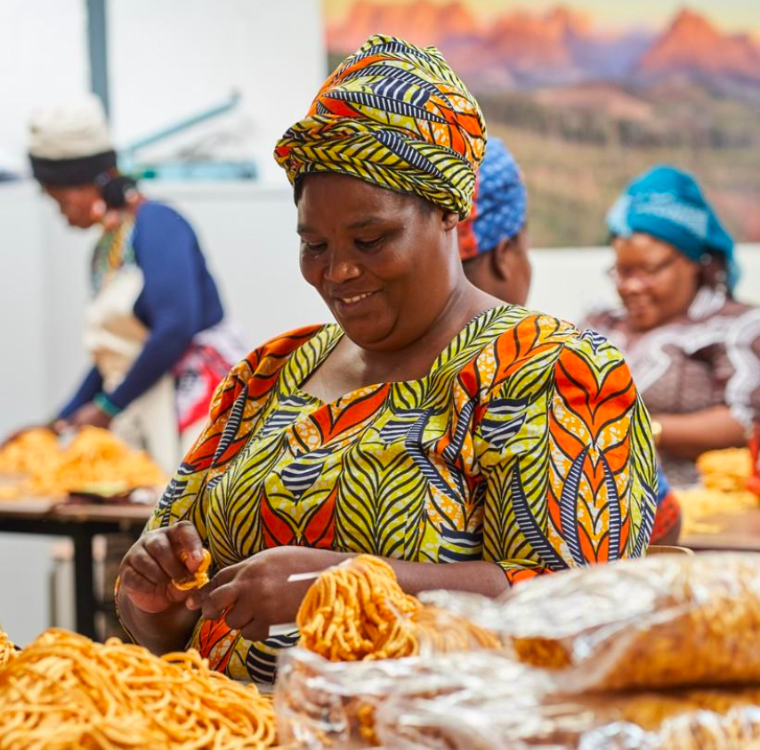 Woman in colorful traditional attire working with food at a market stall.
