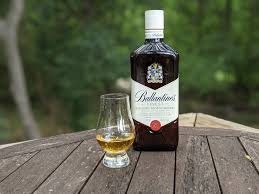 Bottle of Ballantine's whisky with a glass on a wooden surface outdoors