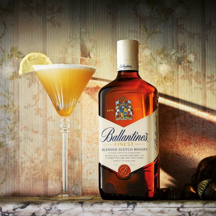 Ballantine's whisky bottle with a cocktail garnished with a lemon slice on a textured background