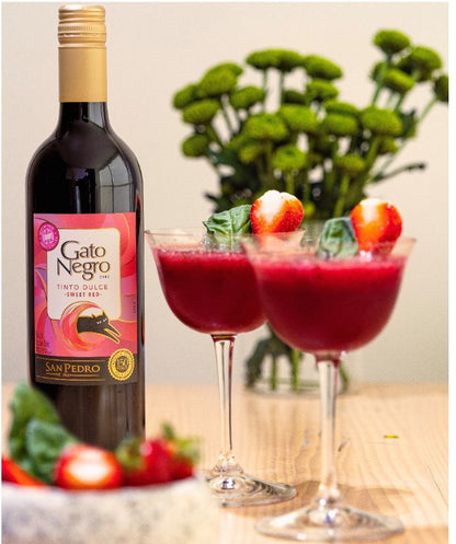 Bottle of Gato Negro wine with two red cocktails on a wooden table.