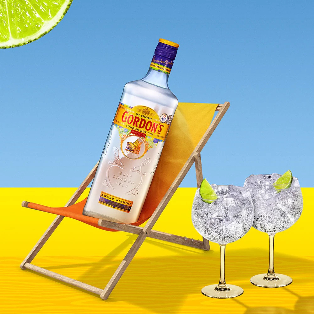 Gordon's gin bottle with two glasses on a bright yellow surface and blue background
