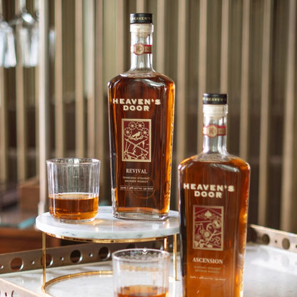 Two bottles of Heaven's Door whiskey with glasses on a marble surface.