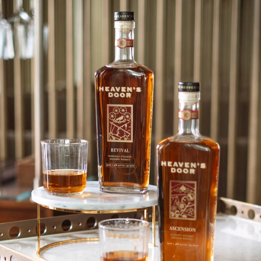 Two bottles of Heaven's Door whiskey with glasses on a marble surface.