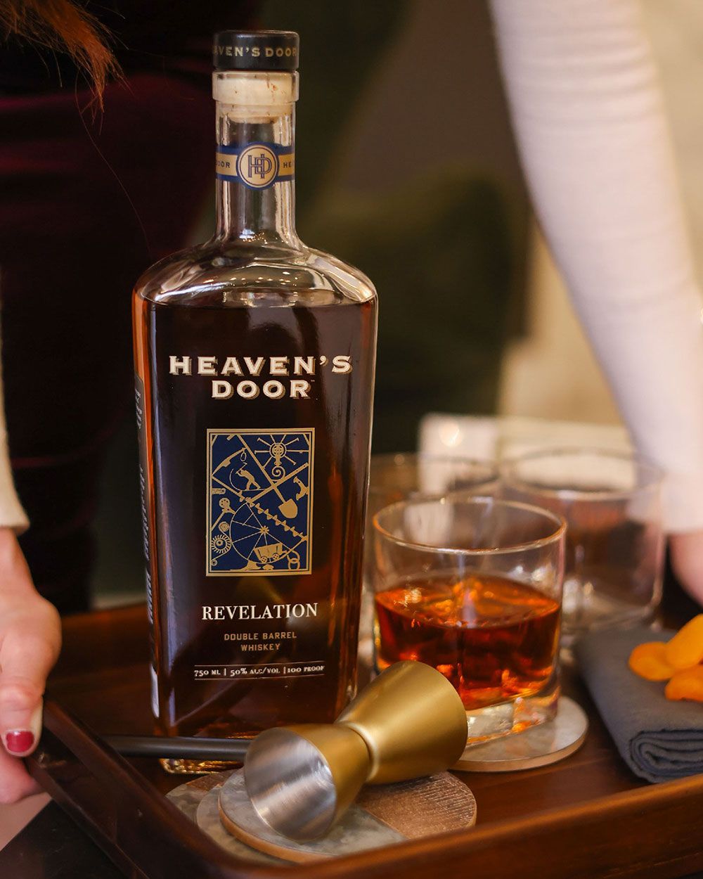 Bottle of Heaven's Door whiskey with a glass of whiskey on a wooden tray.