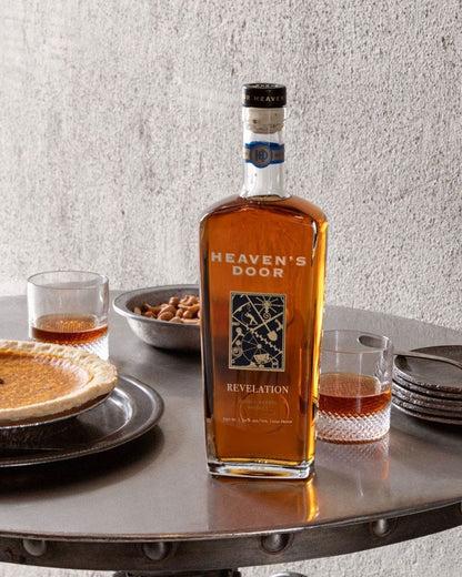 Bottle of Heaven's Door Revelation bourbon on a table with pie and glasses.