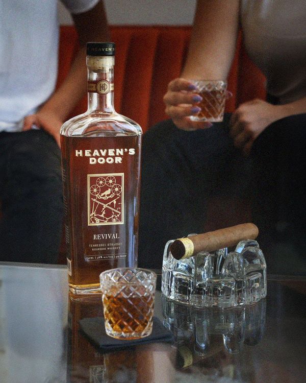 Heaven's Door whiskey bottle with glasses and a cigar on a table