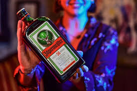 Person holding a bottle of Jägermeister liqueur with a colorful background