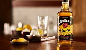 Jim Beam Honey whiskey bottle on a wooden surface with lemons and glasses in the background