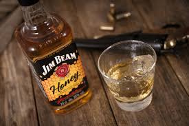 Jim Beam Honey whiskey bottle with a glass of whiskey on a wooden surface