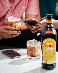 Two people sitting at a table with drinks and a bottle of Kahláu.