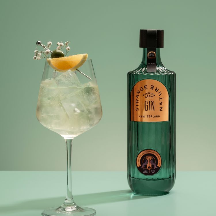 Bottle of Strange Nectar Gin with a cocktail garnished with a slice of lemon and ice cubes on a green background