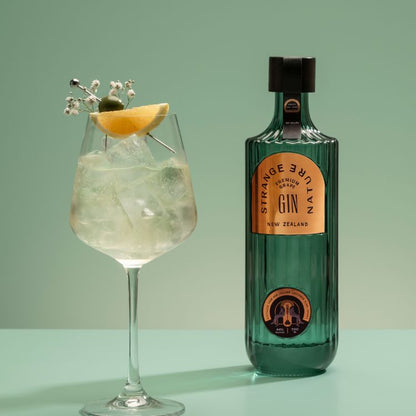 Bottle of Strange Nectar Gin with a cocktail garnished with a slice of lemon and ice cubes on a green background